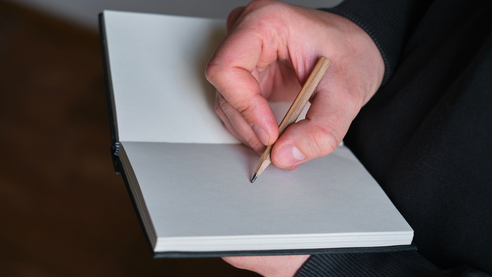 A student's hand sketching a messy pencil diagram in a spiral notebook under warm desk lamp light.